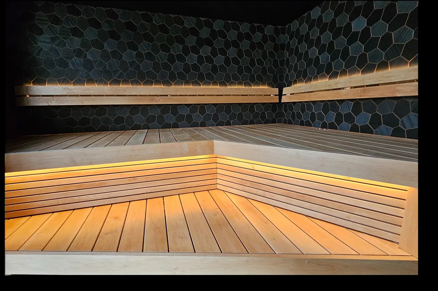 A sauna room with black hexagonal panels and soft bench lighting